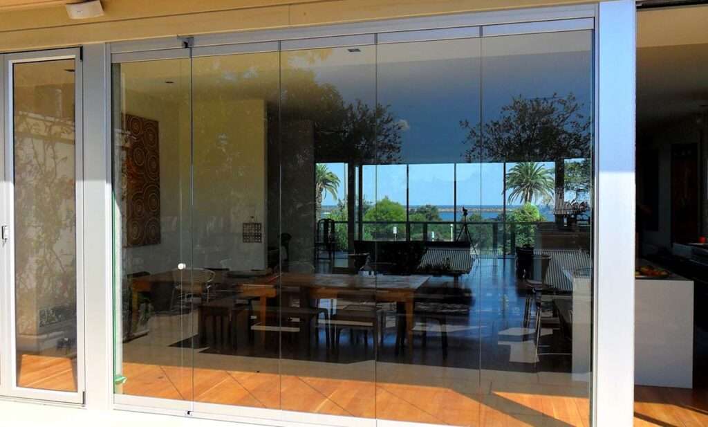 A luxurious living room with frameless bi-fold doors, fully opened to create a seamless transition between indoor and outdoor spaces, enhancing natural light and modern aesthetics.