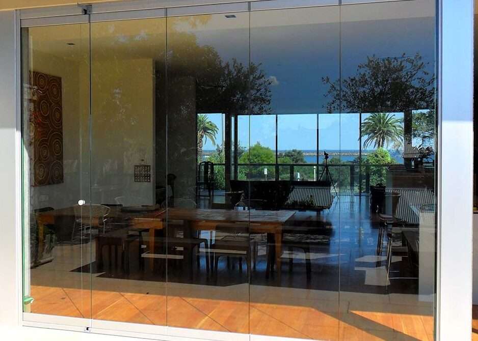A luxurious living room with frameless bi-fold doors, fully opened to create a seamless transition between indoor and outdoor spaces, enhancing natural light and modern aesthetics.