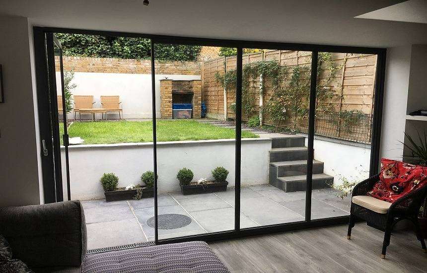 A modern living space with ultra-slim bi-fold doors, fully opened to connect the interior with an outdoor patio, maximizing natural light and providing a sleek, space-saving solution.